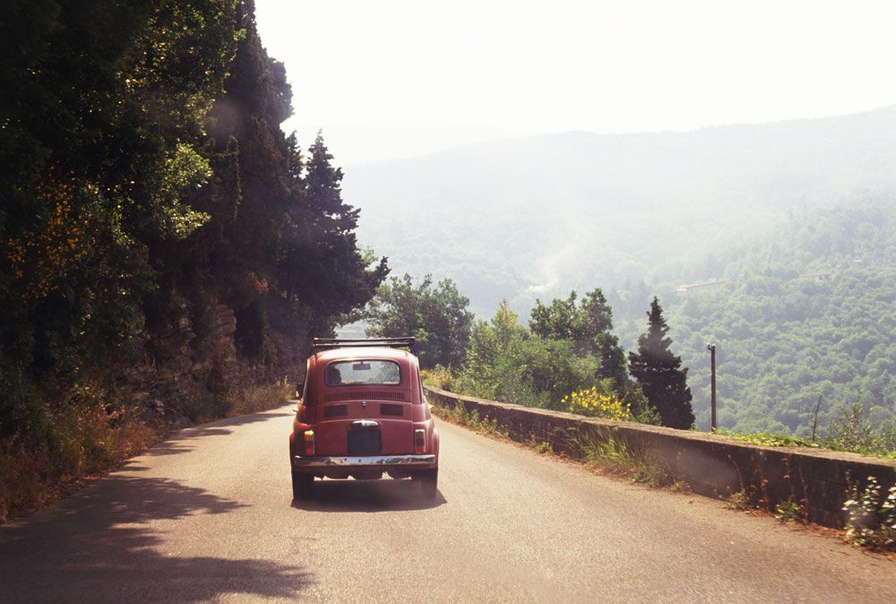 Italy, Eastern Tuscany, nr Borgo San Lorenzo, small red car travelling on mountain road, view from behind