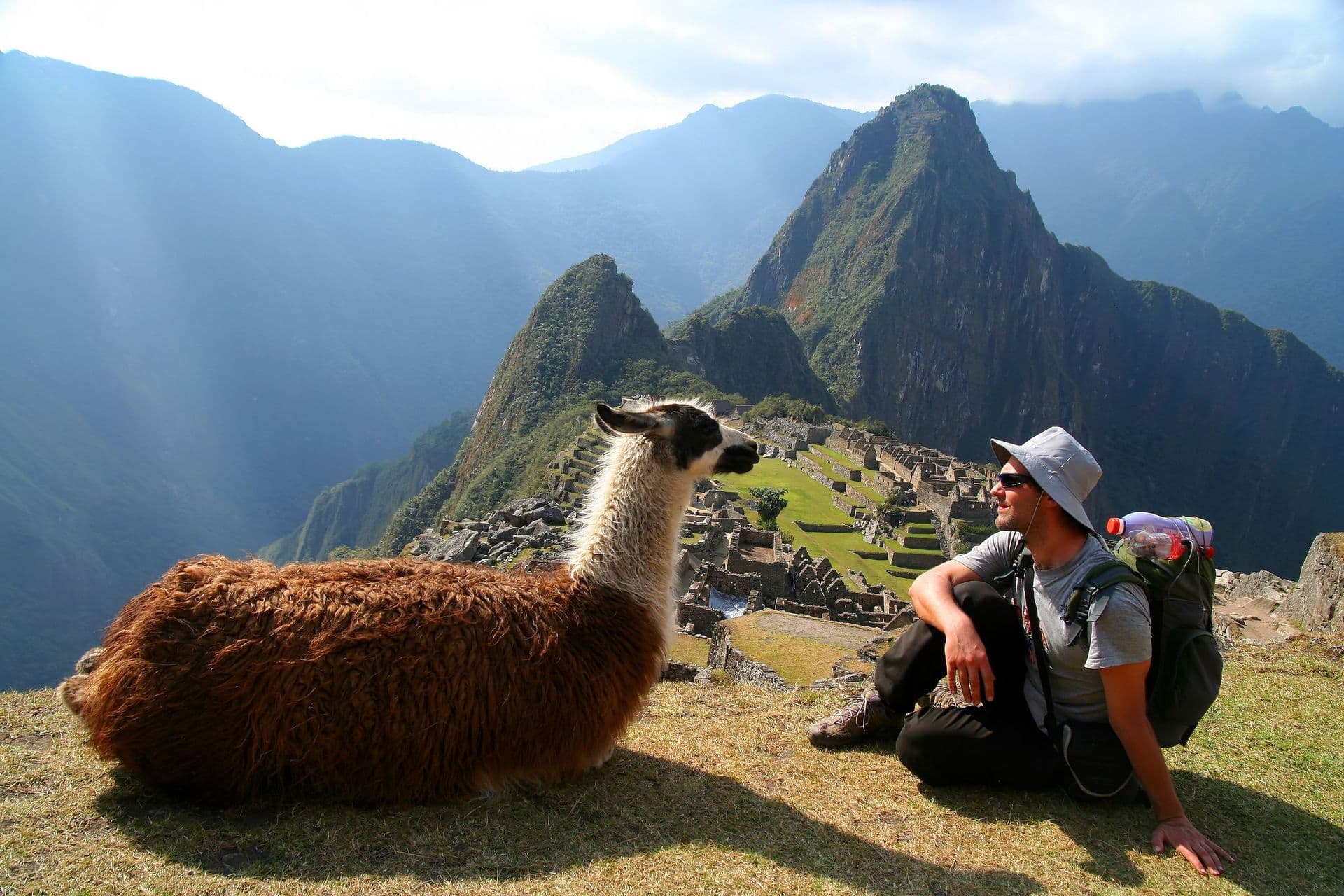 Tourist and llama sitting in front of Machu Picchu, Peru