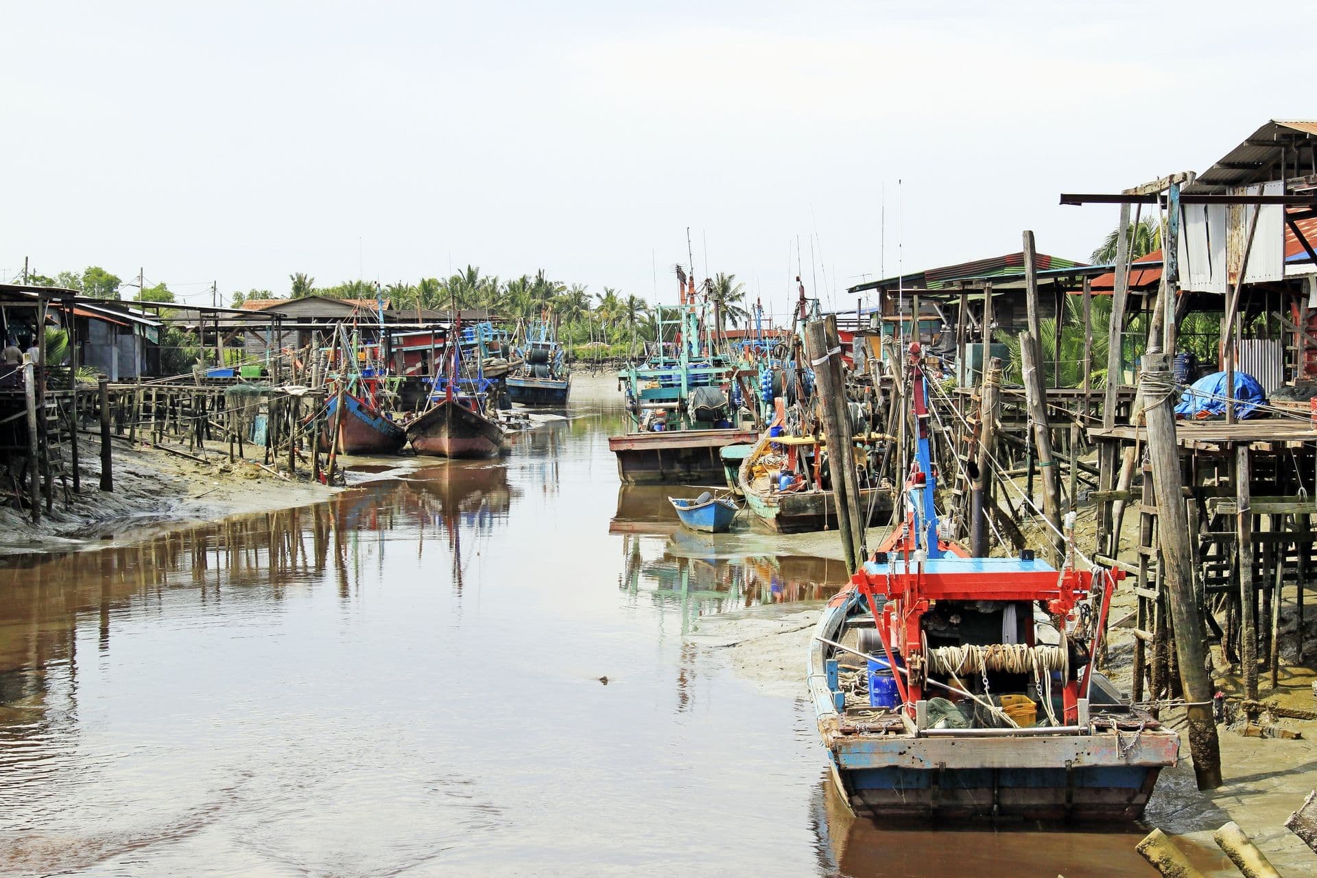 A landscape view of a remote rural fishing village in Kuala Selangor district of Malaysia with fishing boat docking at the river pier during low tide.