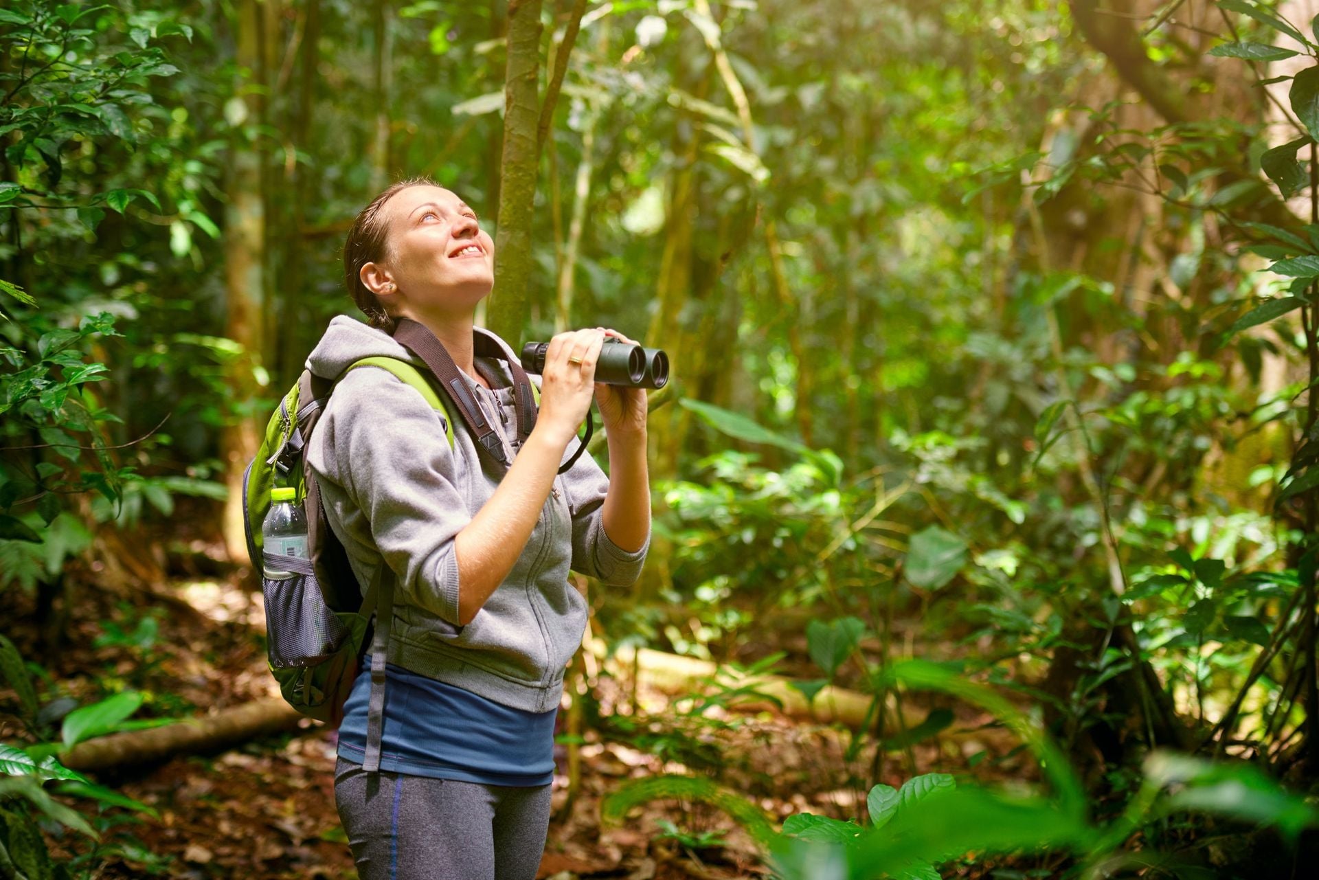 Hiker watching through binoculars wild birds in the jungle.