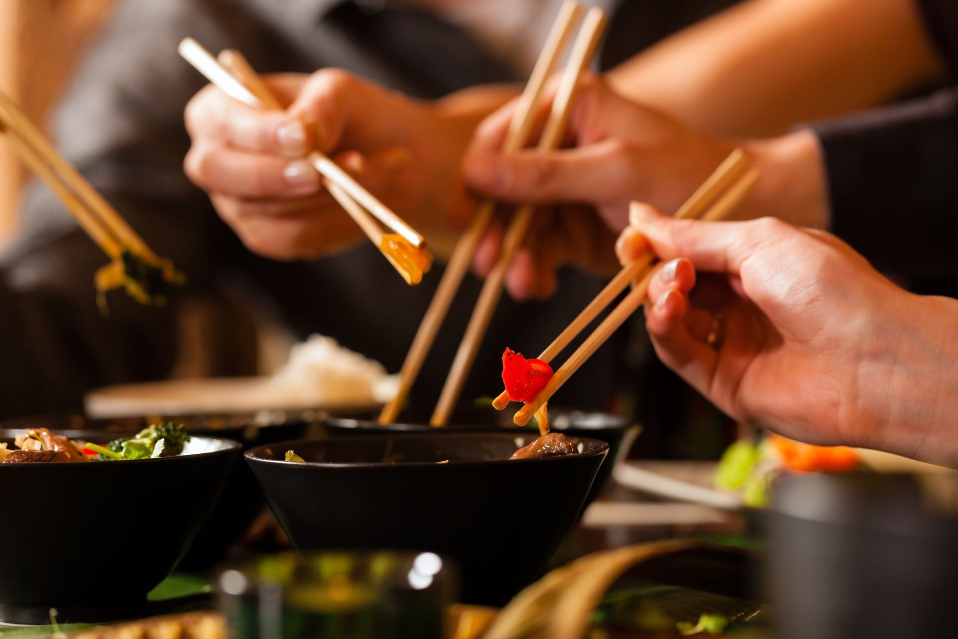 Young people eating in a Thai restaurant, they eating with chopsticks, close-up on hands and food