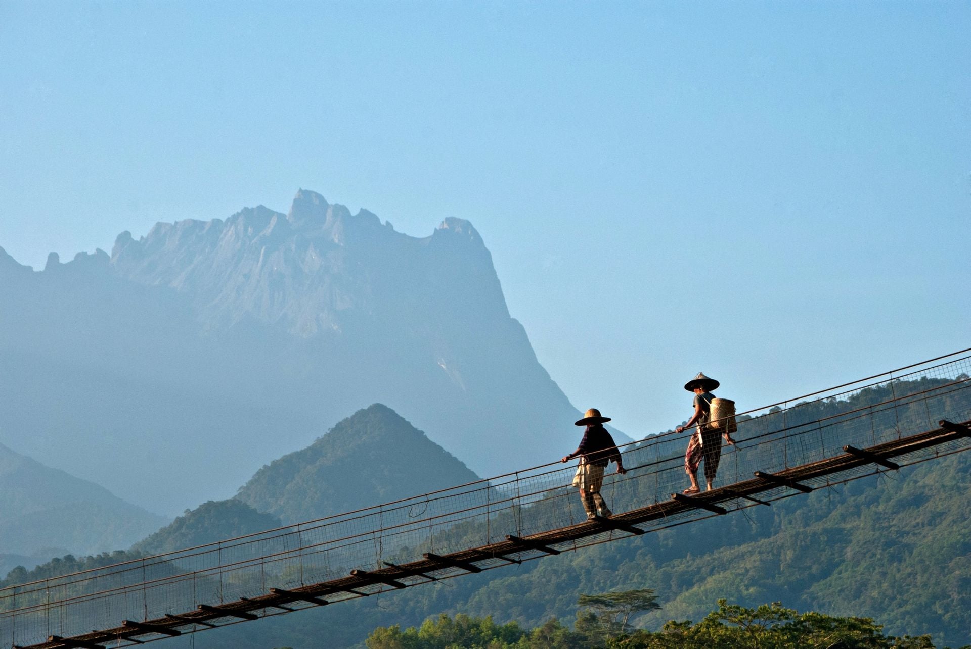 Two unidentified couple of elderly farmers at Kota Belud, Sabah are walking on a suspension bridge on an early morning, with Mount Kinabalu as background