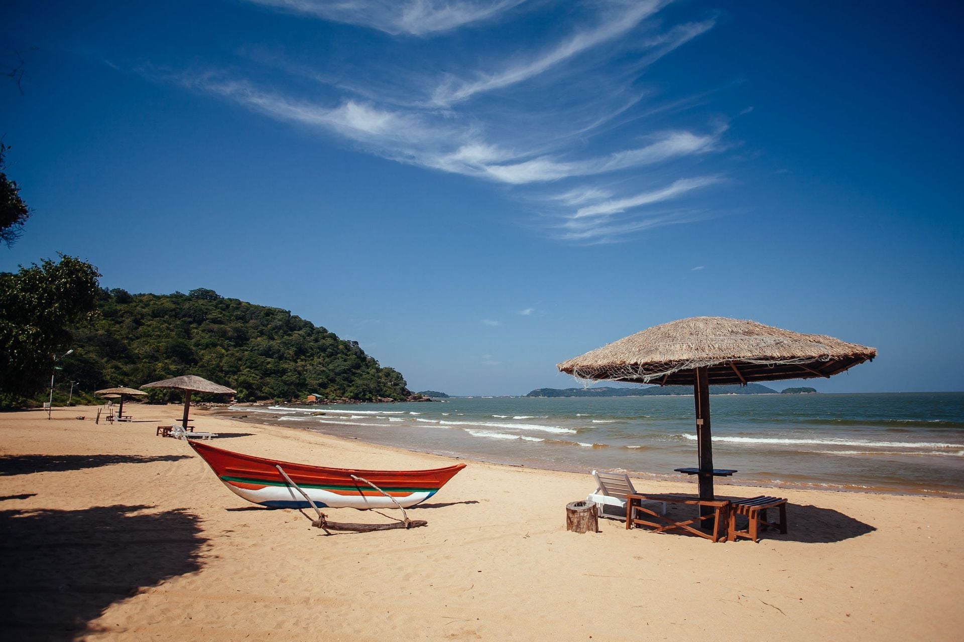 Beach umbrella on sand next to tropical lagoon. Sun umbrellas and boats on Marble beach, Sri Lanka, Trincomalee