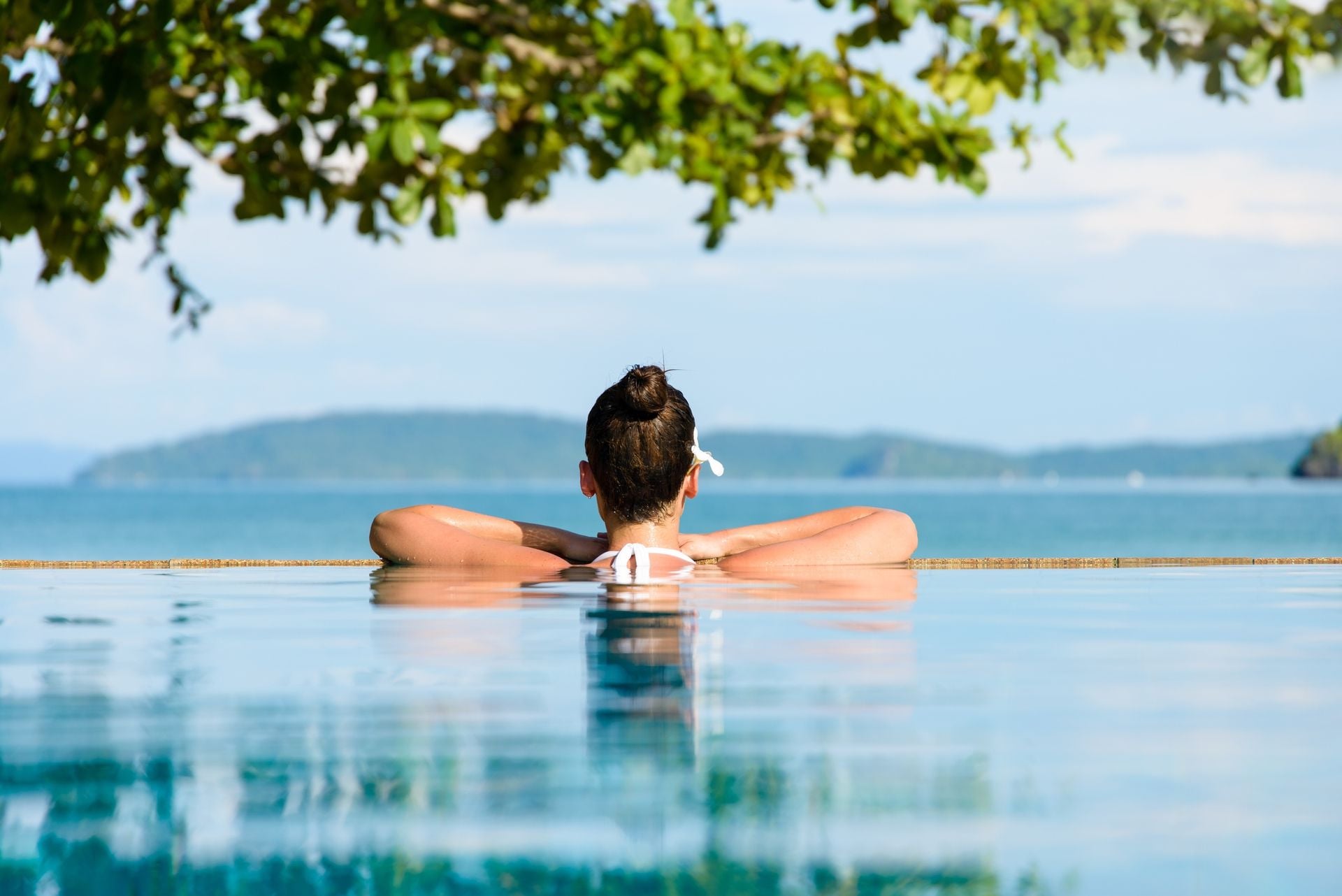 Relax and spa concept. Woman with a flower in hair relaxing in a pool towards the sea at Krabi, Thailand.