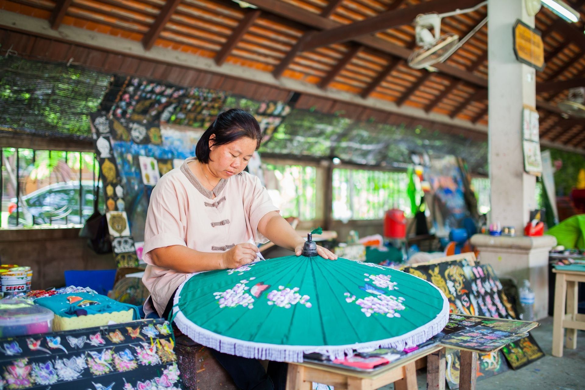 old asian Woman sitting, painting green wooden umbrella in traditional umbrella factory