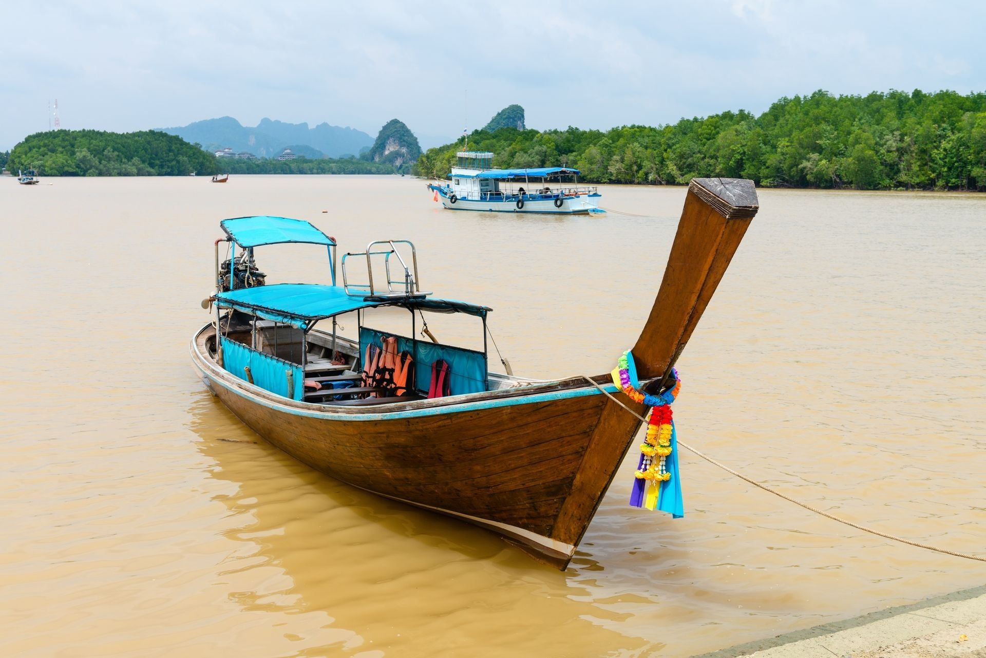 Traditional wooden decorated boat on tropical river with Krabi landmark (Khao Kanab Nam cliff) on background, Krabi Town, Thailand