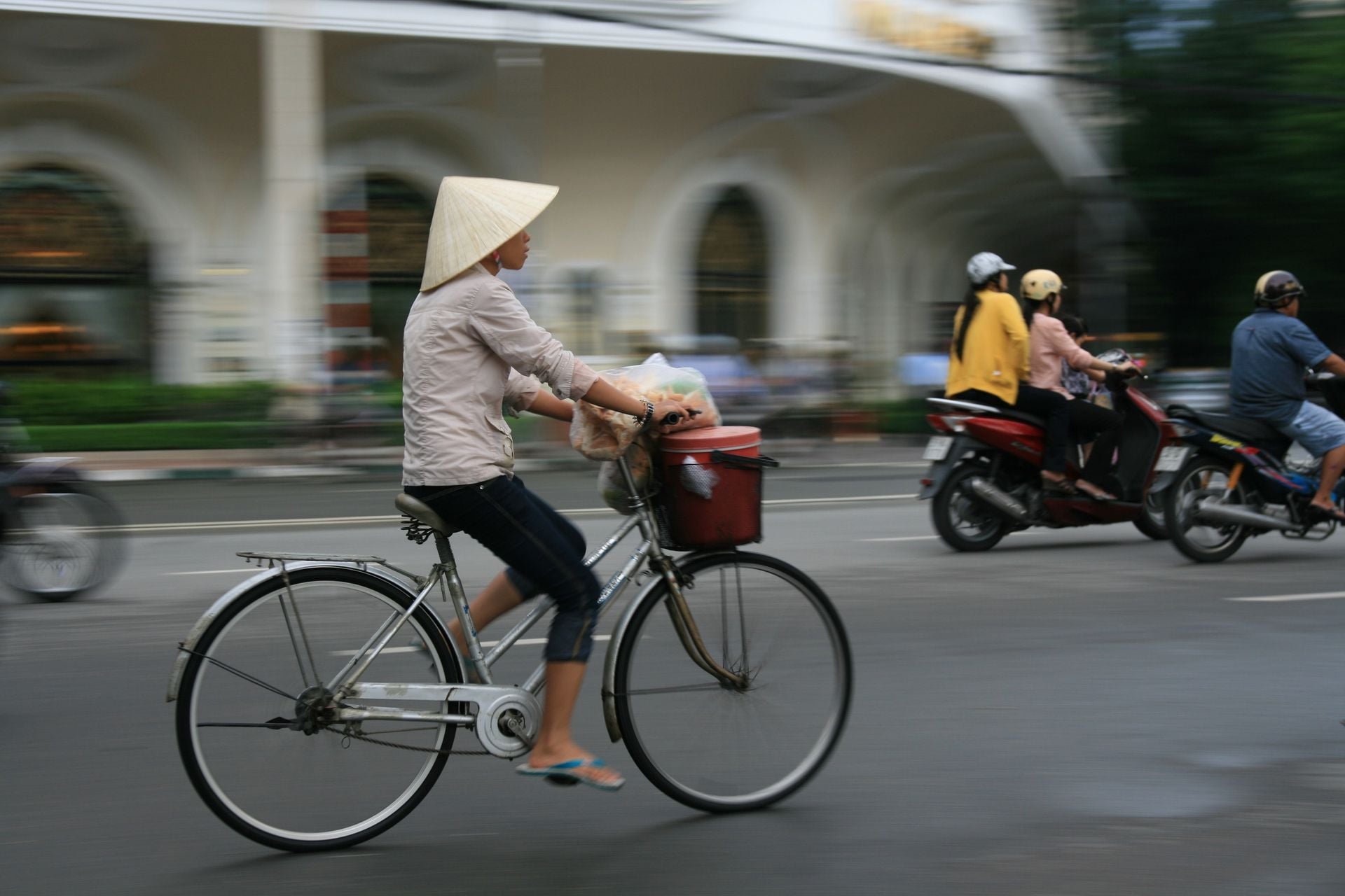 Woman cycling on busy Hanoi Roadwith traditional Vietnamese hat