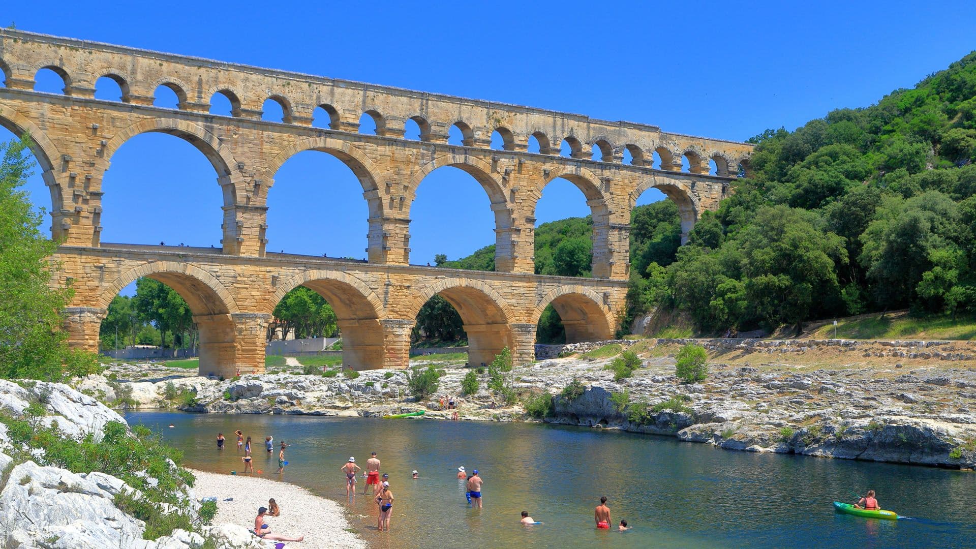 Ancient arches of Pont du Gard and people swimming on the river near Nimes, France