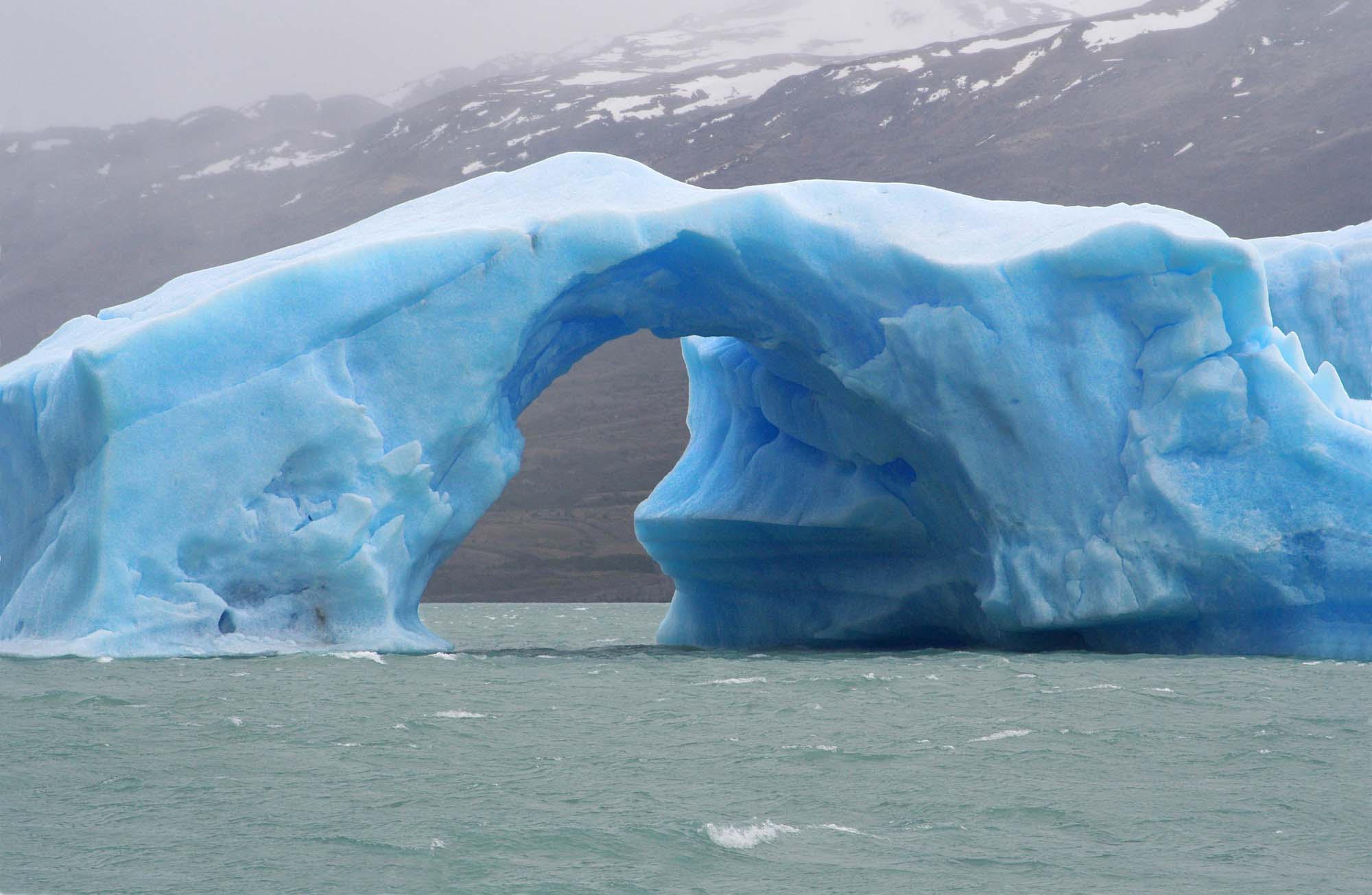 iceberg with an arch of ice floating in argentino lake, in the argentinian national park of glaciers