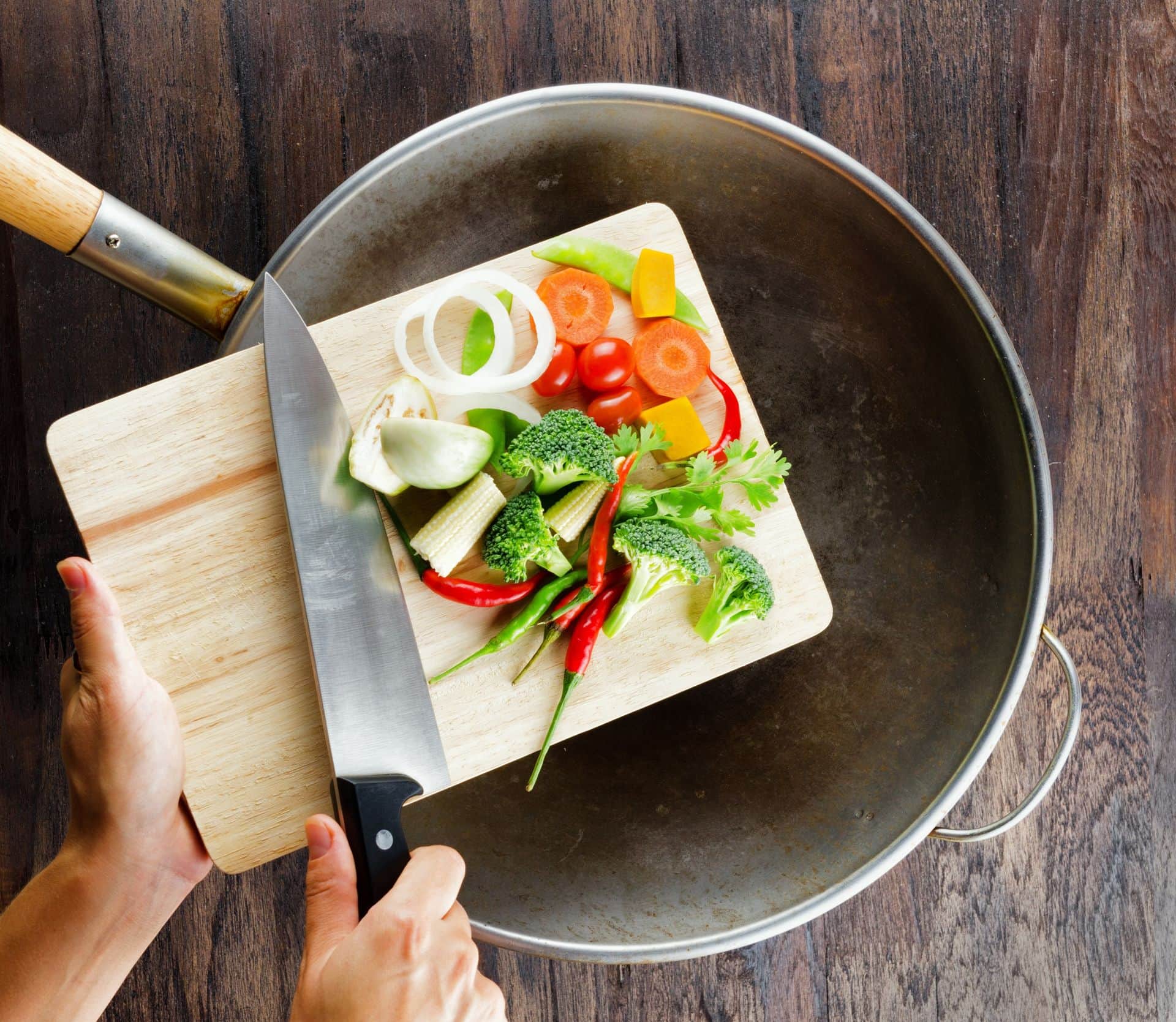 Fresh vegetables on the cutting board are falling in the wok. Concept of cooking.