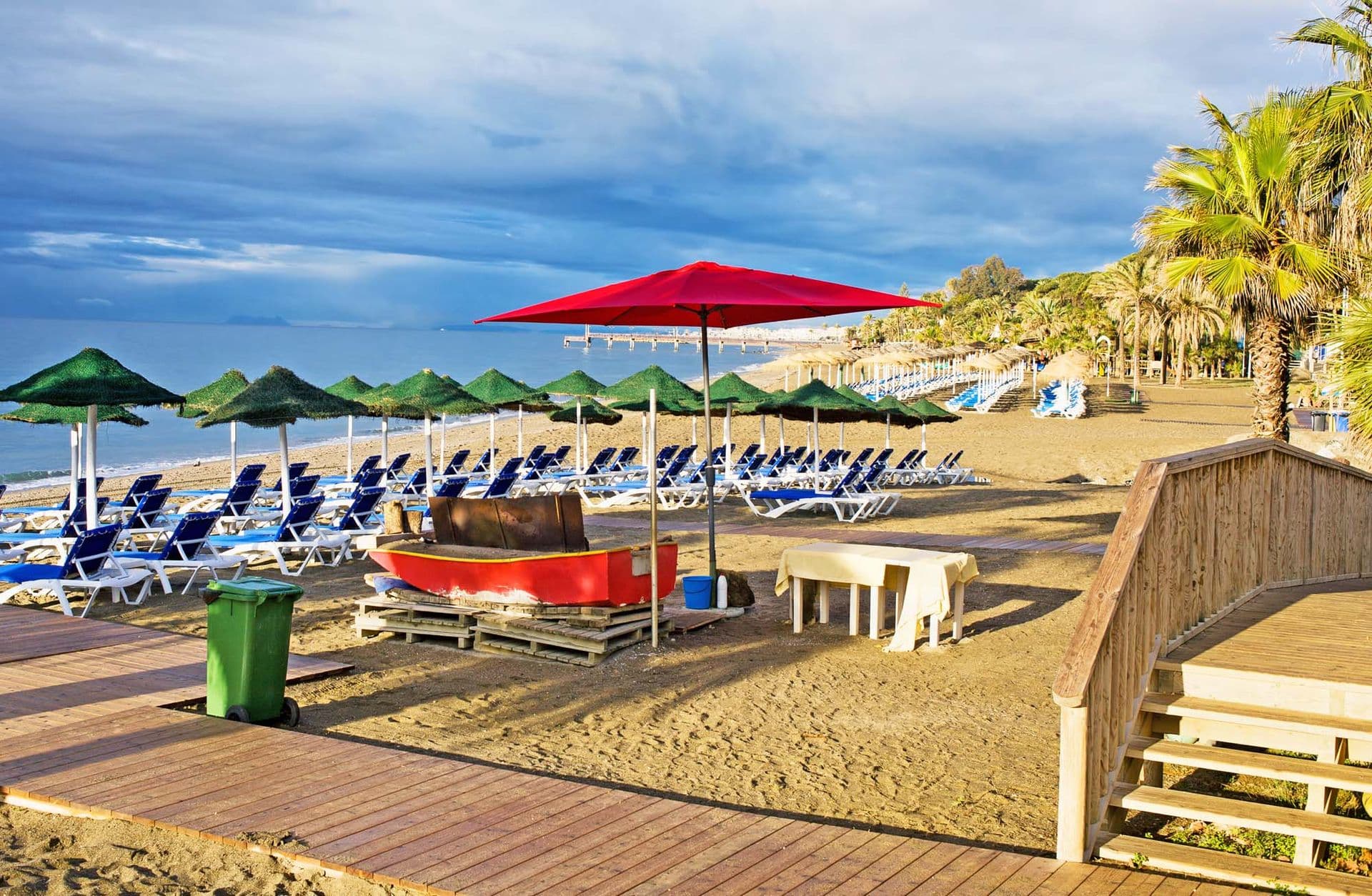 Sun loungers with umbrellas on a beach in the morning at popular resort of Marbella in Spain, Costa del Sol, Andalusia region.