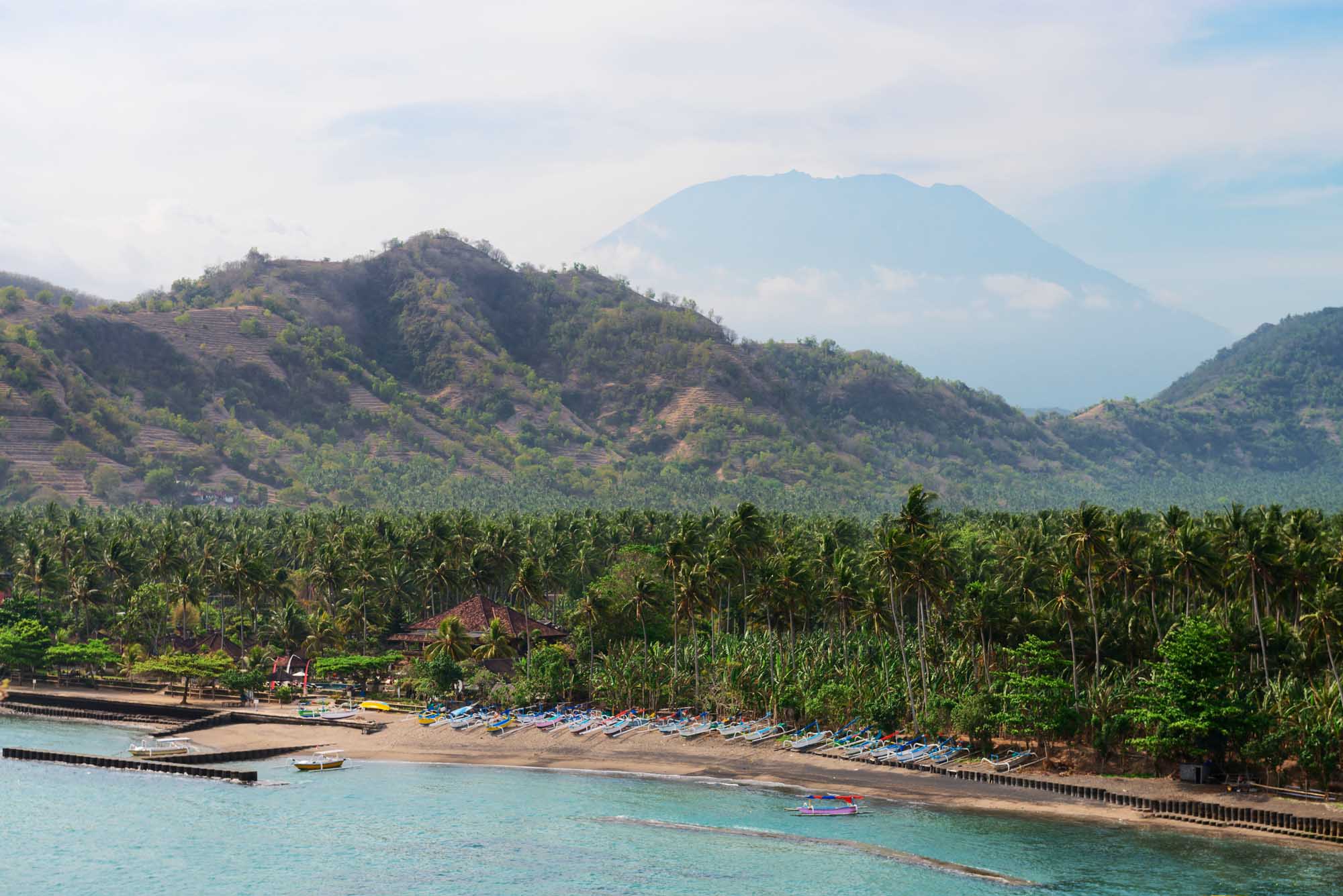 Tropical beach with palms and boats and big volcano on background on Bali in Candidasa