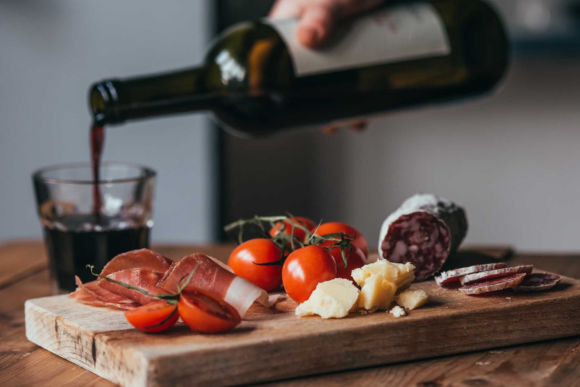 Appetizers - tomato, meat and cheese - on wooden board with bottle of wine and glass.