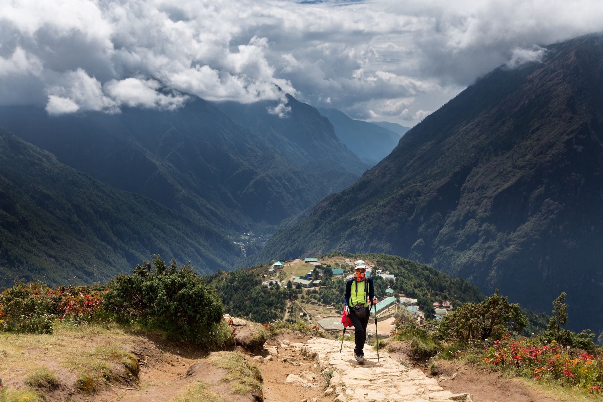 Young female backpacker walking hiking mountain trail footpath high above Namche Bazaar village houses, Nepal.