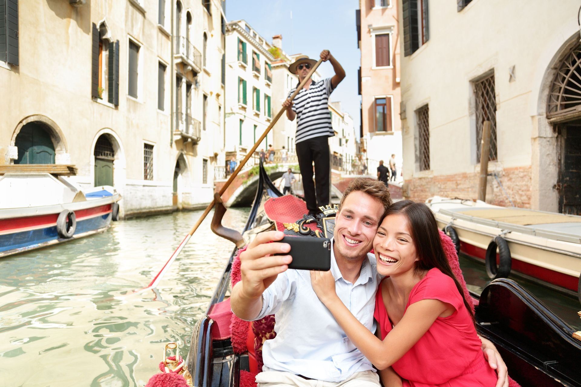 Travel couple taking selfie picture in gondola on Venice vacation. Beautiful lovers on a romantic boat ride across the Venetian canals taking self-portrait pictures with smartphone during holiday.