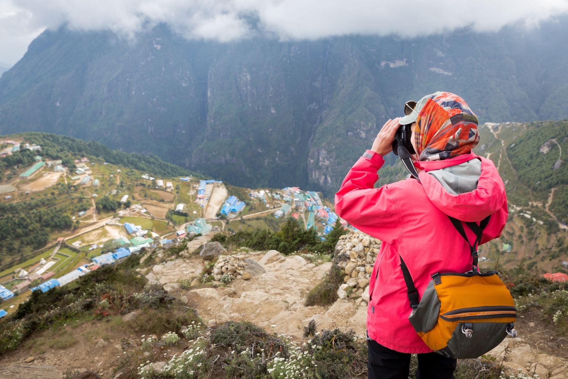 Young female photographer tourist standing above mountain village taking pictures buildings, Namche Bazaar, Nepal.