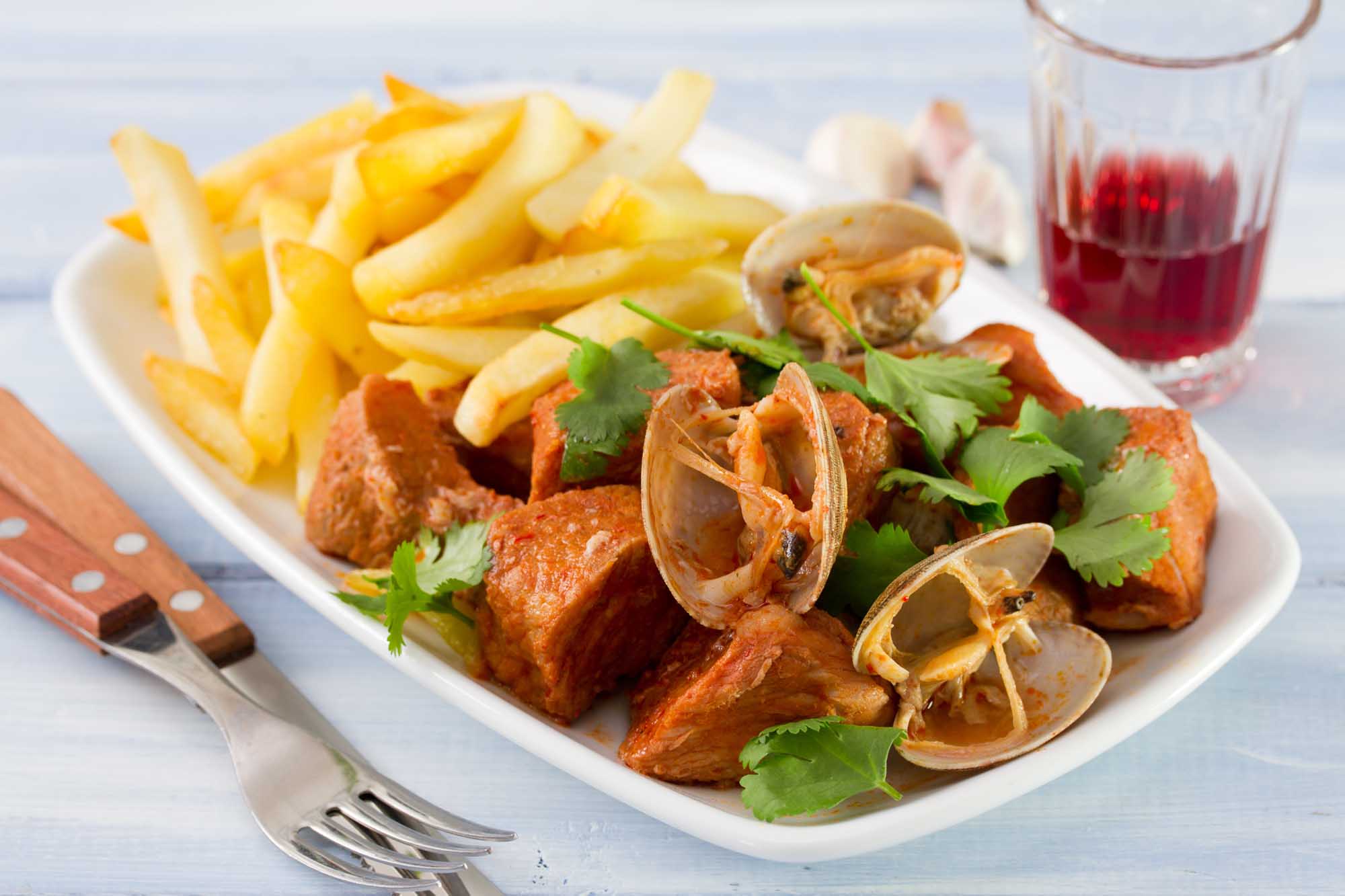 typical portuguese dish Carne de Porco a Alentejana on dish and glass of red wine
