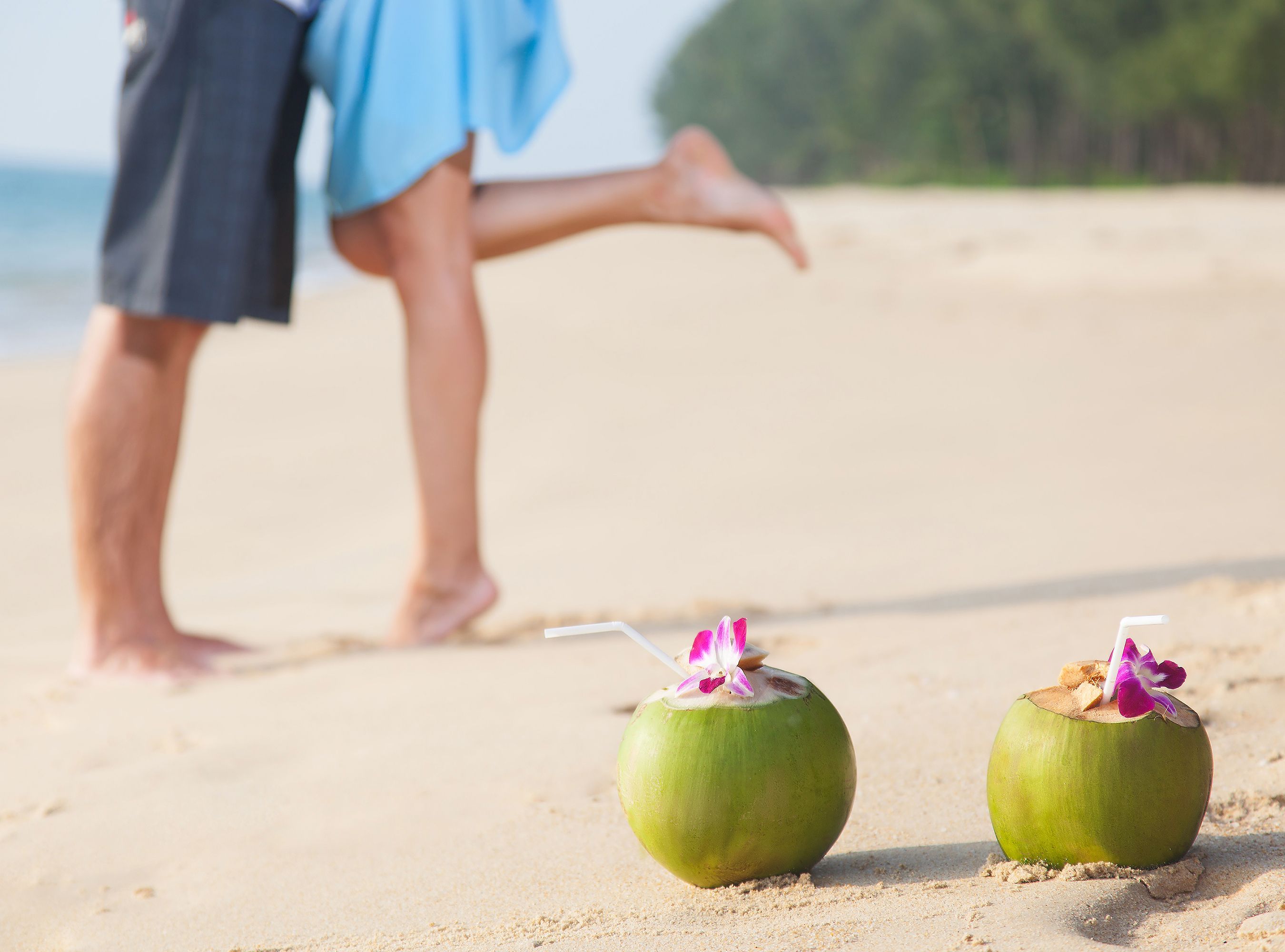 Two coconuts on the beach with couple on the background. Focus on the coconuts.