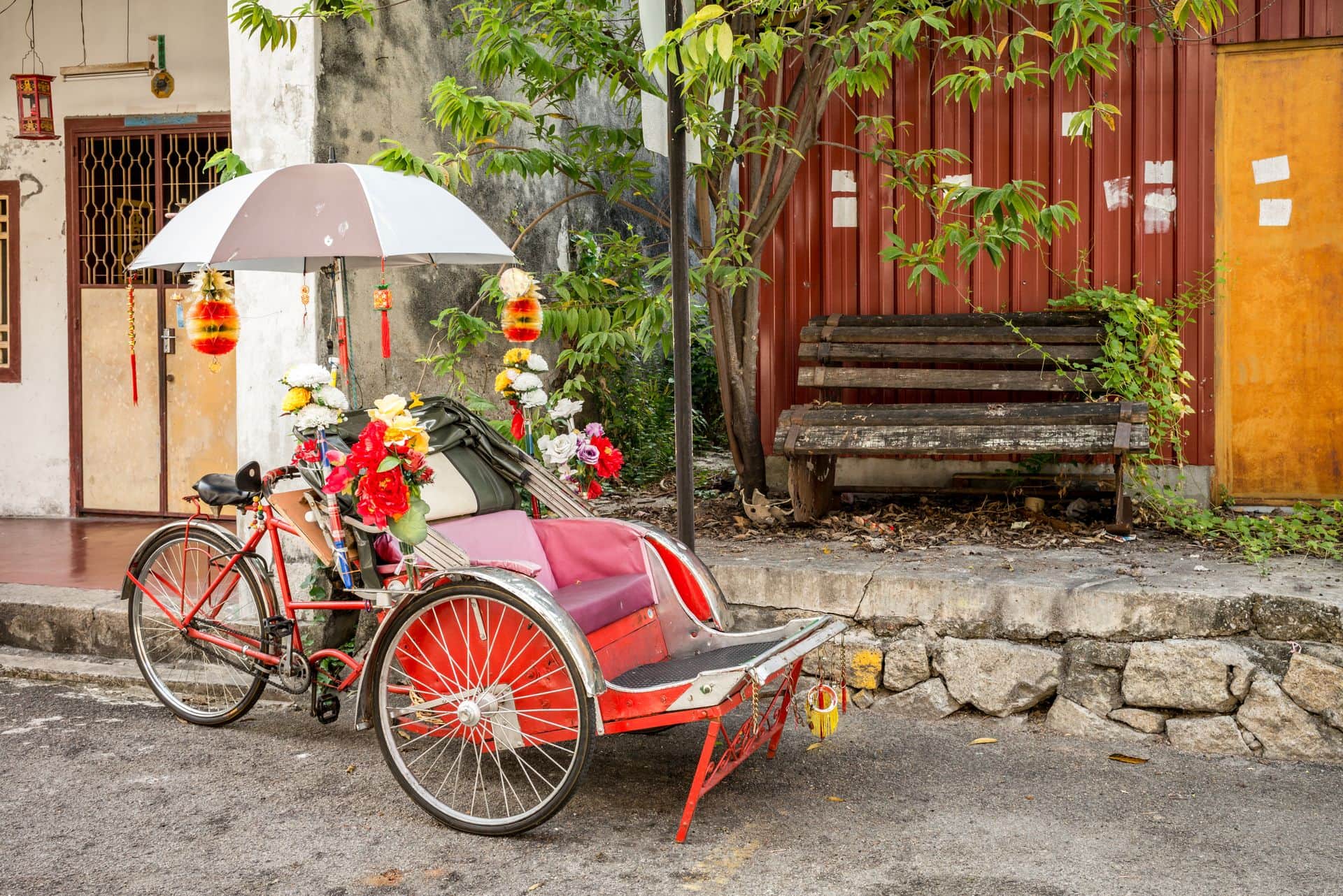 An old rickety trishaw cab parked on the sidewalk of a dilapidated building in Penang, Malaysia.