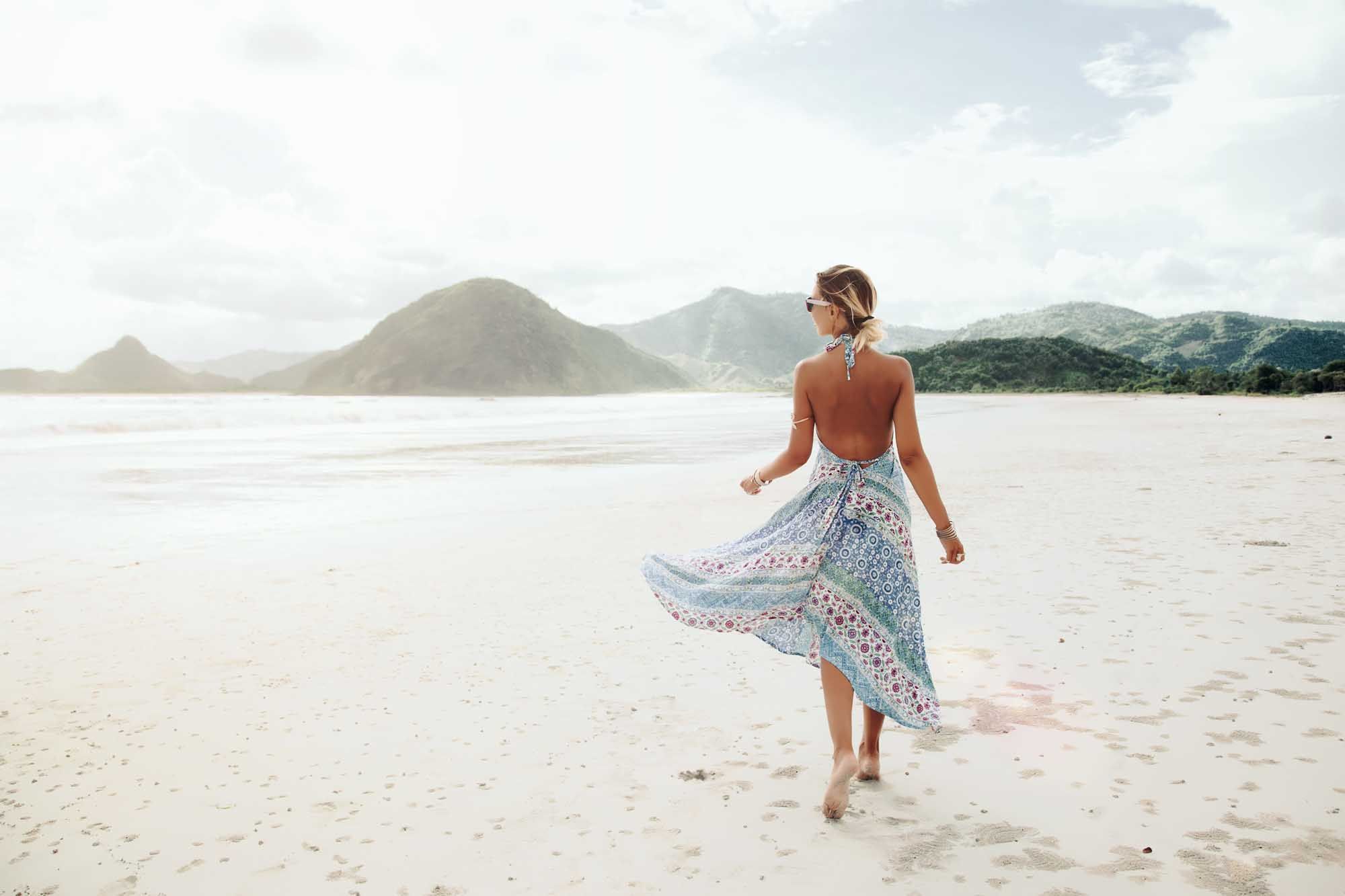 Woman wearing ethnic flying dress walking barefoot at the beach, Lombok, Indonesia