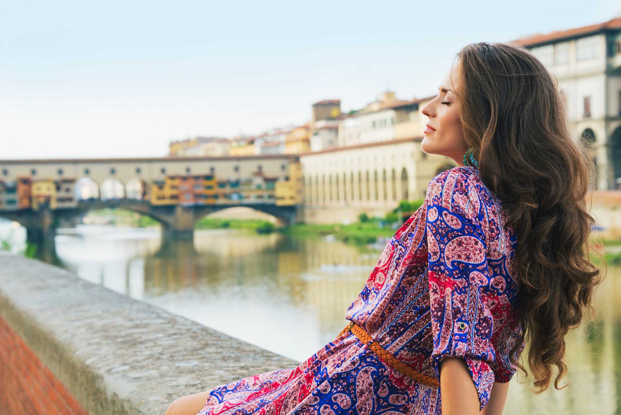 Relaxed young woman in a dress sitting on the embankment near Ponte Vecchio