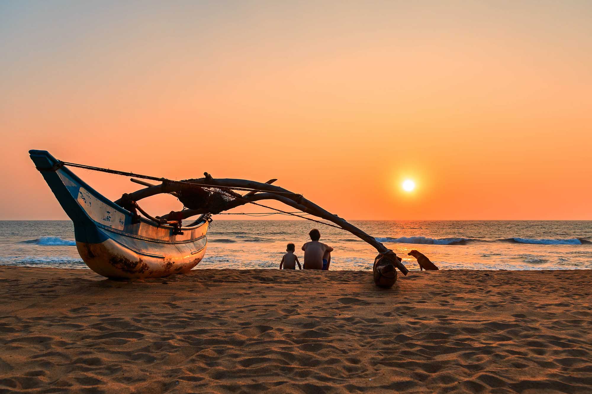 Young man and boy, father and son, dog sitting on the beach at sunset, Kalutara, Sri Lanka