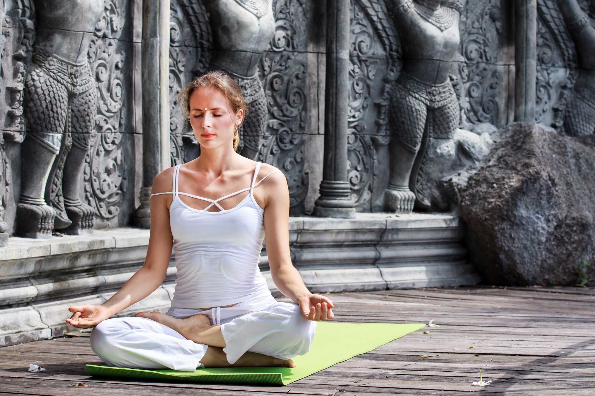 Young woman doing yoga in abandoned temple on wooden platform. Practicing.