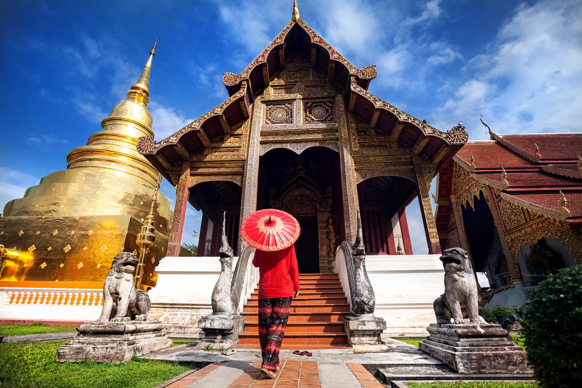 Woman tourist with red traditional Thai umbrella near Golden temple Wat Phra Singh in Chiang Mai, Thailand